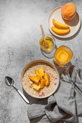 Oatmeal with peaches and nuts  in a bowl on a gray background with honey