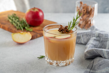 Apple cider with cinnamon, anise, and rosemary in glass on a light background