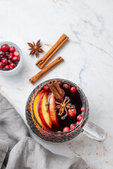 Fototapeta premium A cup of hot mulled wine with spices, orange and apple slices, cinnamon on a marble background