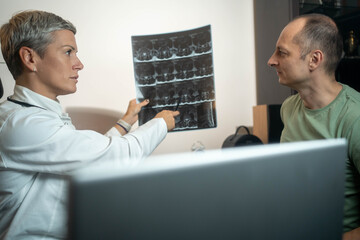 Confident female doctor discussing spinal MRI scan results with patient during professional healthcare consultation.	