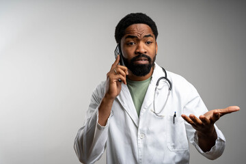 African doctor talking on phone and looking at camera in clinic, isolated background, copy space
