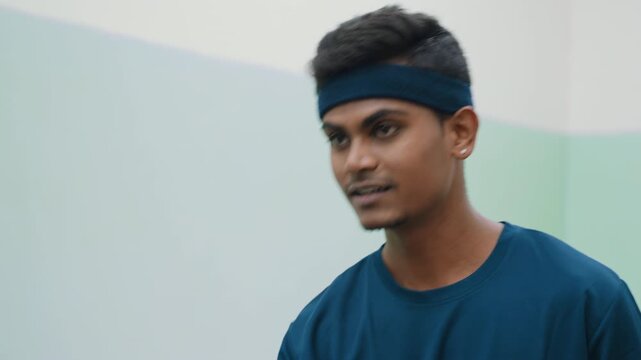 man in blue shirt and headband concentrating while repeatedly attempting to balance tennis ball in air using breath, focused expression showing determination and persistence during playful moment