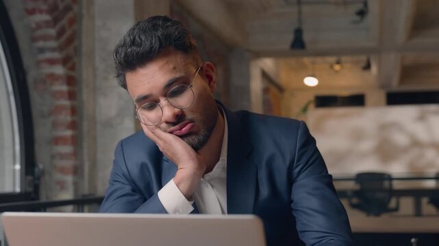 Bored lazy unmotivated Arabian businessman Hindu business man working laptop in office suffering with boring job task typing computer tired guy male frustrated upset depressed burnout problem boredom