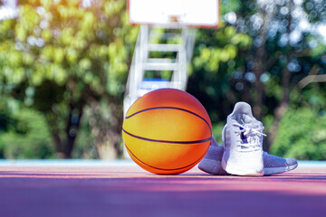 An orange basketball and a pair of white athletic shoes rest on an outdoor court.