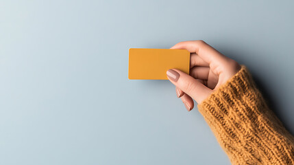 A hand in a cozy knit sleeve holds a golden rectangular object against a soft blue backdrop, offering a visual invitation to add your own message or promotion.