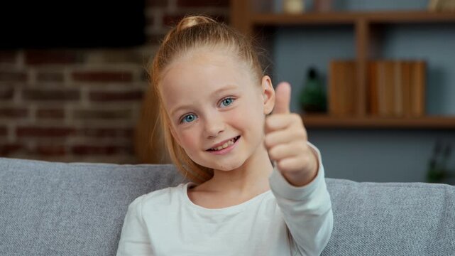 Portrait Caucasian happy child girl showing like kid daughter show thumb up at home looking at camera smiling satisfied joyful recommend positive good choice emotion agree yes sign enjoy family adopt