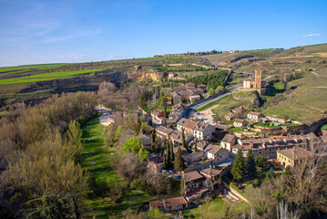 A picturesque view overlooks the Segovia Templar Church of Vera Cruz in a hilly valley, surrounded by a small village of brown-roofed houses below