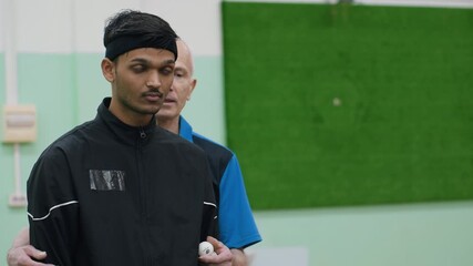 Senior coach in blue shirt demonstrates technique to young athlete in black jacket, showing proper grip and guidance during table tennis training session - Powered by Adobe