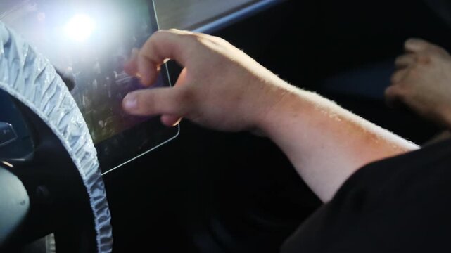 Man hand taps digital tablet screen sitting inside car salon closeup. Driver plans route and riding style with computer technology in modern vehicle