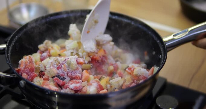 A dish with meat fillet and pieces of frozen vegetables is being prepared in a frying pan. Cooking a stew with rice and vegetables.