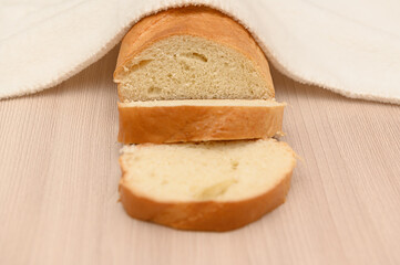 A delicious crispy loaf of bread under a white towel on a wooden table.