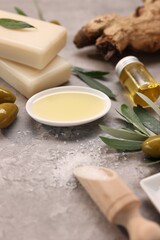 Handmade soap bars, olives, green leaves, oil and sea salt on gray textured table, closeup