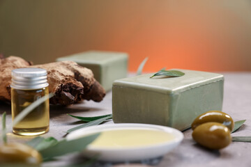 Handmade soap bars, olives, green leaves and oil on gray table, closeup