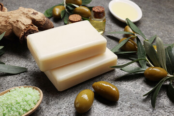 Handmade soap bars, olives, green leaves, sea salt and oil on gray textured background, closeup