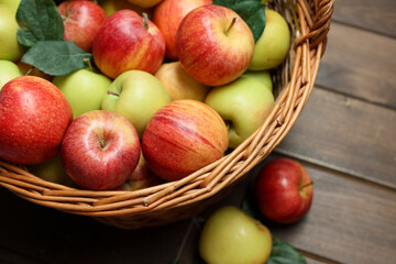 Fresh apples in wicker basket and green leaves on wooden table, above view