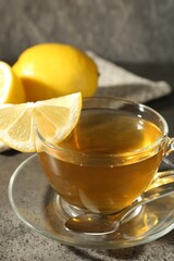 Aromatic tea in cup with lemons and spoon on grey table, closeup