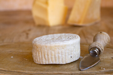 fresh goat cheese wheel with wooden knife on rustic cutting board artisan dairy product closeup