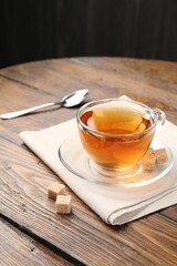 Aromatic black tea in glass cup and brown sugar on wooden table, closeup