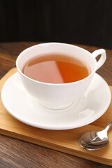 Aromatic black tea in cup and spoon on wooden table, closeup