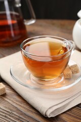 Aromatic black tea in glass cup, brown sugar and teapot on wooden table, closeup