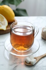 Aromatic black tea in glass cup, sugar and lemons on white marble table, closeup