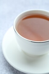 Aromatic black tea in cup on light grey table, closeup