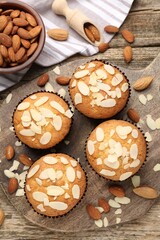 Tasty muffins with almond flakes and nuts on wooden table, flat lay