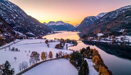 Obraz premium Aerial view of lake amidst snow covered valley with mountain backdrop under an orange and purple colored sky