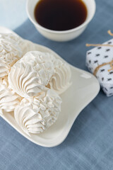 Delicate meringue cookies arranged on a white plate beside a cup of dark coffee, showcasing a sweet treat perfect for dessert lovers and coffee enthusiasts
