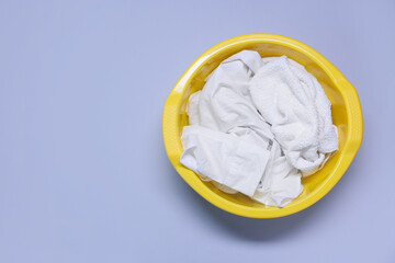 Plastic basin with clothes on light purple background, top view. Space for text