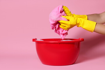 Woman washing clothes in plastic basin on pink background, closeup. Space for text