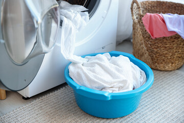 Plastic basin with laundry near washing machine in bathroom, closeup