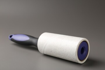 Lint roller with used sticky tape on grey background, closeup
