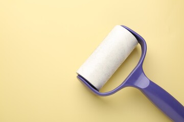 Lint roller with used sticky tape on yellow background, top view. Space for text
