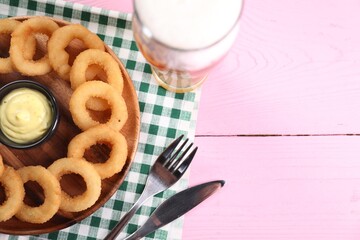 Fried squid rings with sauce and beer served on pink wooden table, flat lay. Space for text