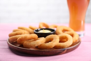 Fried squid rings with sauce and beer served on pink wooden table, closeup