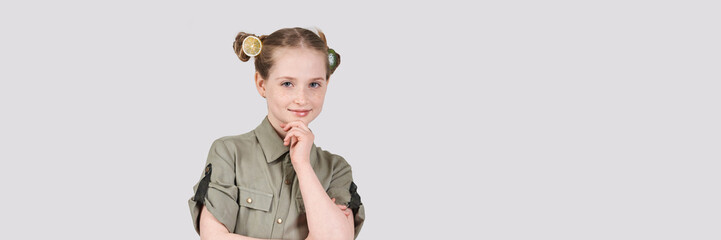 Caucasian female child with lemon hair accessories and green shirt smiling against plain background.