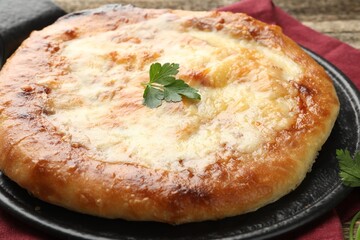Delicious Megrelian khachapuri with parsley on wooden table, closeup
