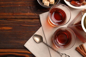 Tasty Turkish tea in glass cups, teapot, brown sugar, dates and cinnamon on wooden table, flat lay. Space for text