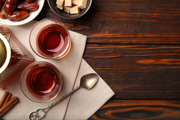 Tasty Turkish tea in glass cups, teapot, brown sugar, dates and cinnamon on wooden table, flat lay. Space for text