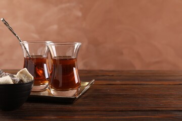 Tasty Turkish tea in glass cups and sweets on wooden table against brown background, closeup. Space for text