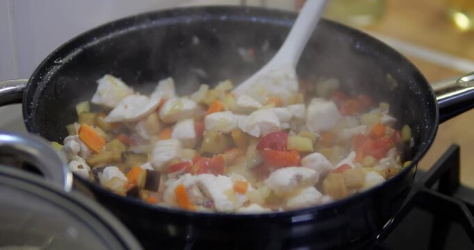 A dish with meat fillet and pieces of frozen vegetables is being prepared in a frying pan. Cooking a stew with rice and vegetables.