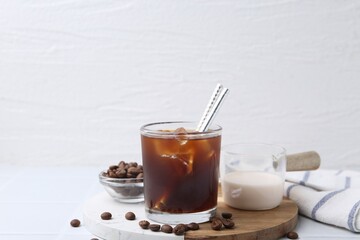 Tasty iced coffee, milk and beans on white table