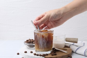 Woman pouring milk into iced coffee at white tiled table, closeup