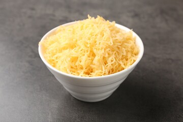 Grated cheese in bowl on grey table, closeup