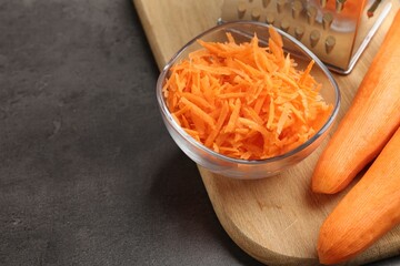 Whole and grated carrots and grater on grey table, closeup. Space for text
