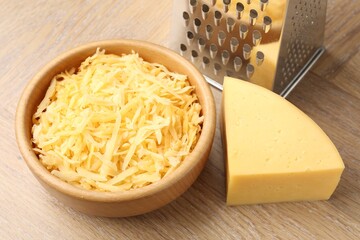Grated and piece of cheese with grater on wooden table, closeup