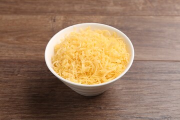 Grated cheese in bowl on wooden table, closeup