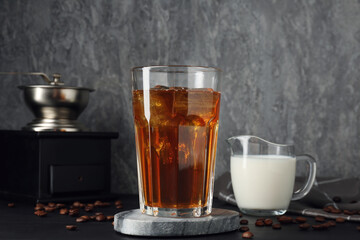 Tasty iced coffee, milk, grinder and beans on black wooden table