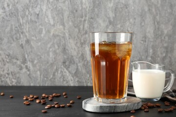 Tasty iced coffee, milk and beans on black wooden table. Space for text